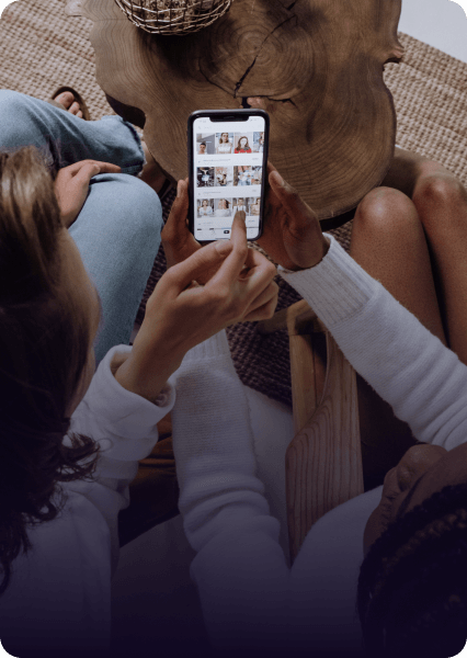 Person holding phone, showing photos to others; soft light, interior setting.