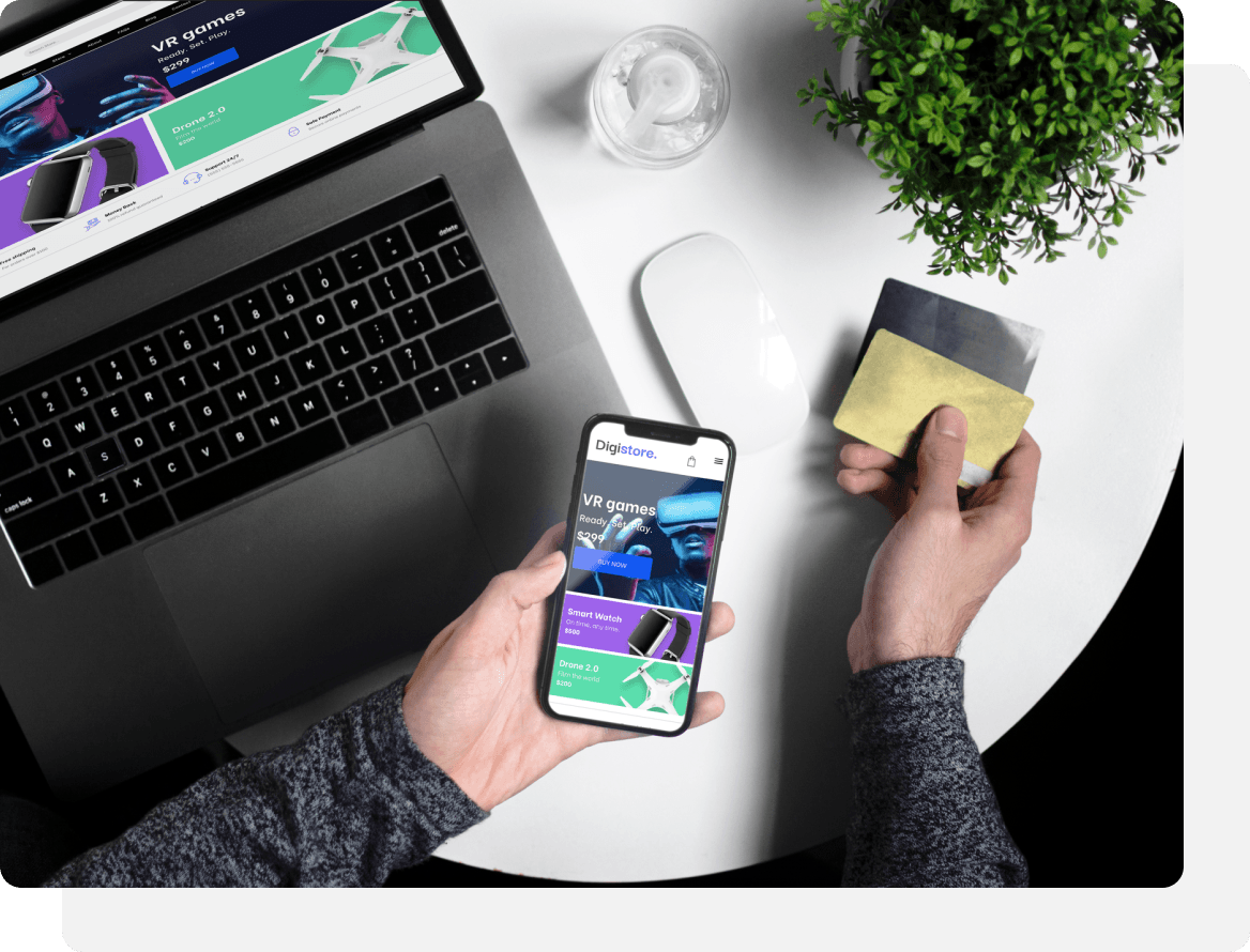 Person holding a phone and credit card, using a laptop at a white table. Plant and glass of water also present.