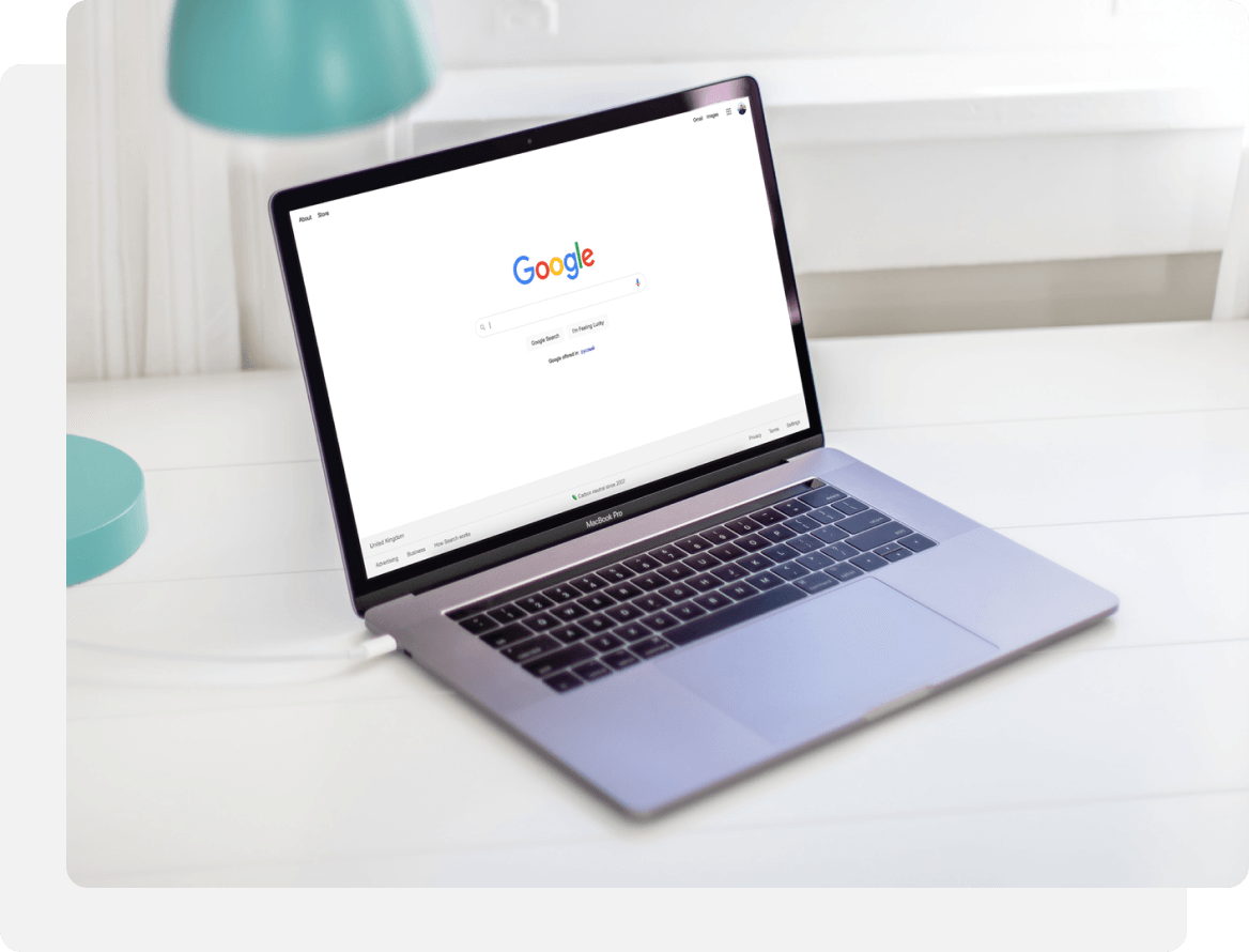 Laptop on a white desk displays Google search page.  A turquoise desk lamp sits nearby.