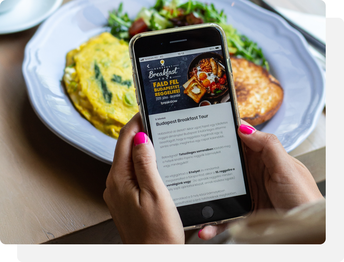 Woman using phone, showing breakfast menu, with food plate in background.
