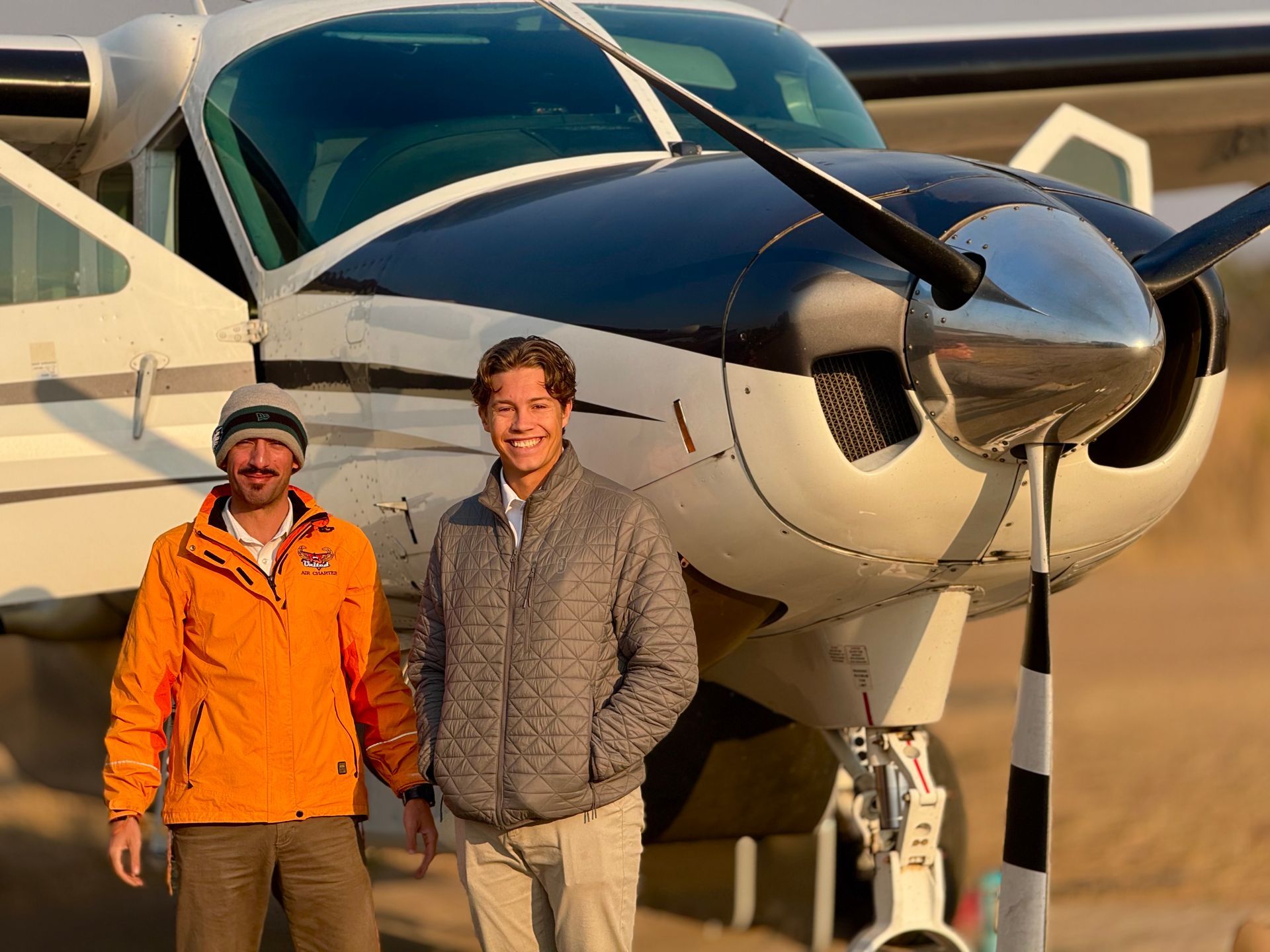 Two men are standing in front of a small plane