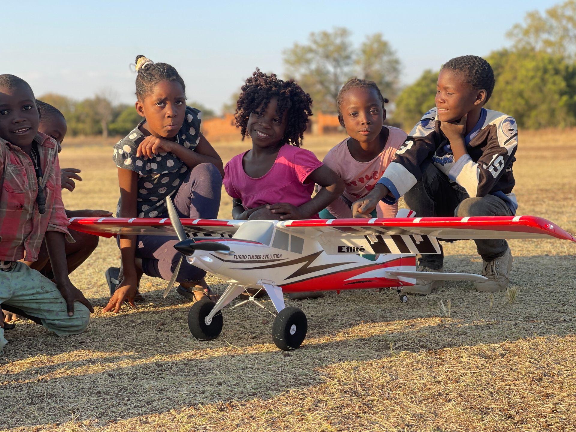 A group of children are sitting around a model airplane.