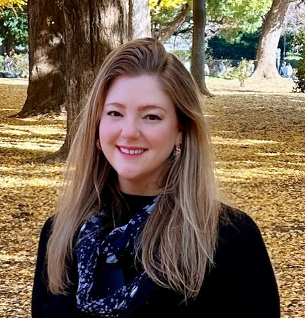 Blonde woman with an orange lip smiles brightly at the camera. Natural light.