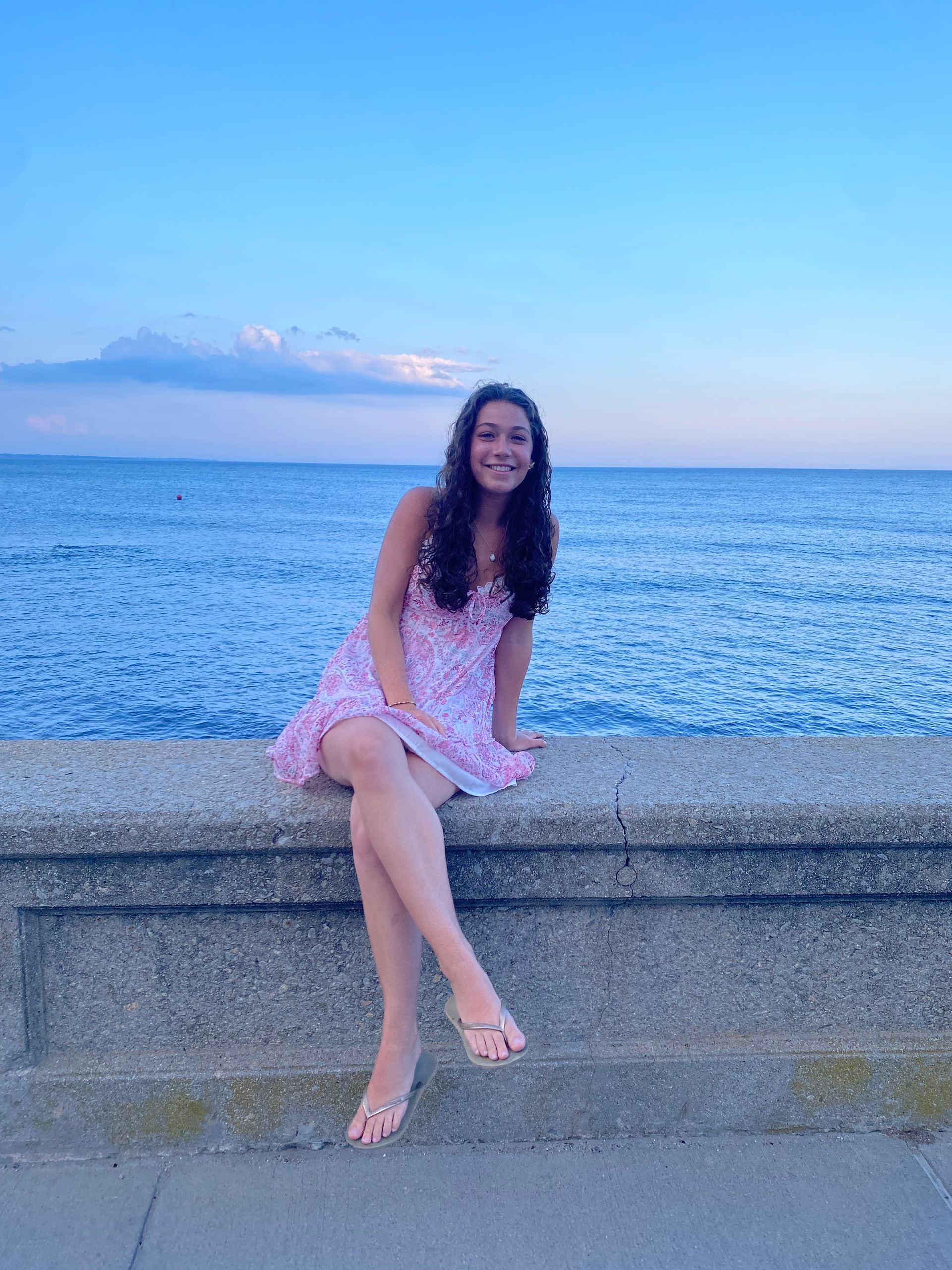Young woman smiles, leaning against a colorful mural. She wears a white top and red pants.