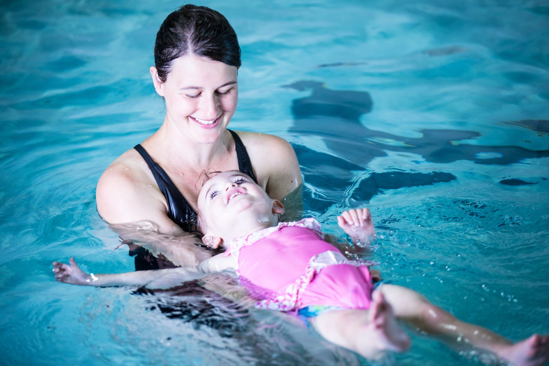 A woman is teaching a baby how to swim in a swimming pool.