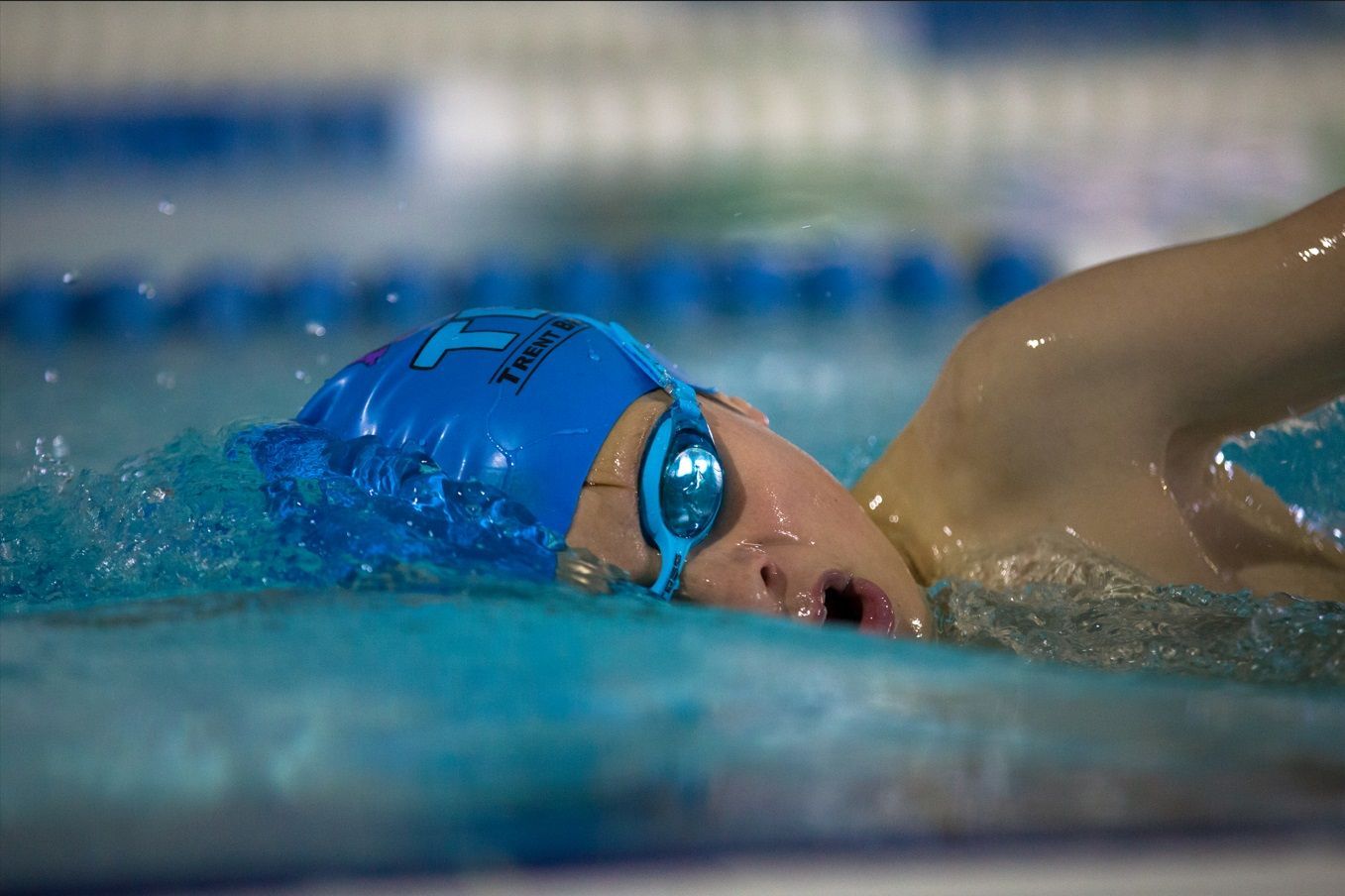 A young boy is swimming in a pool wearing a blue cap and goggles.