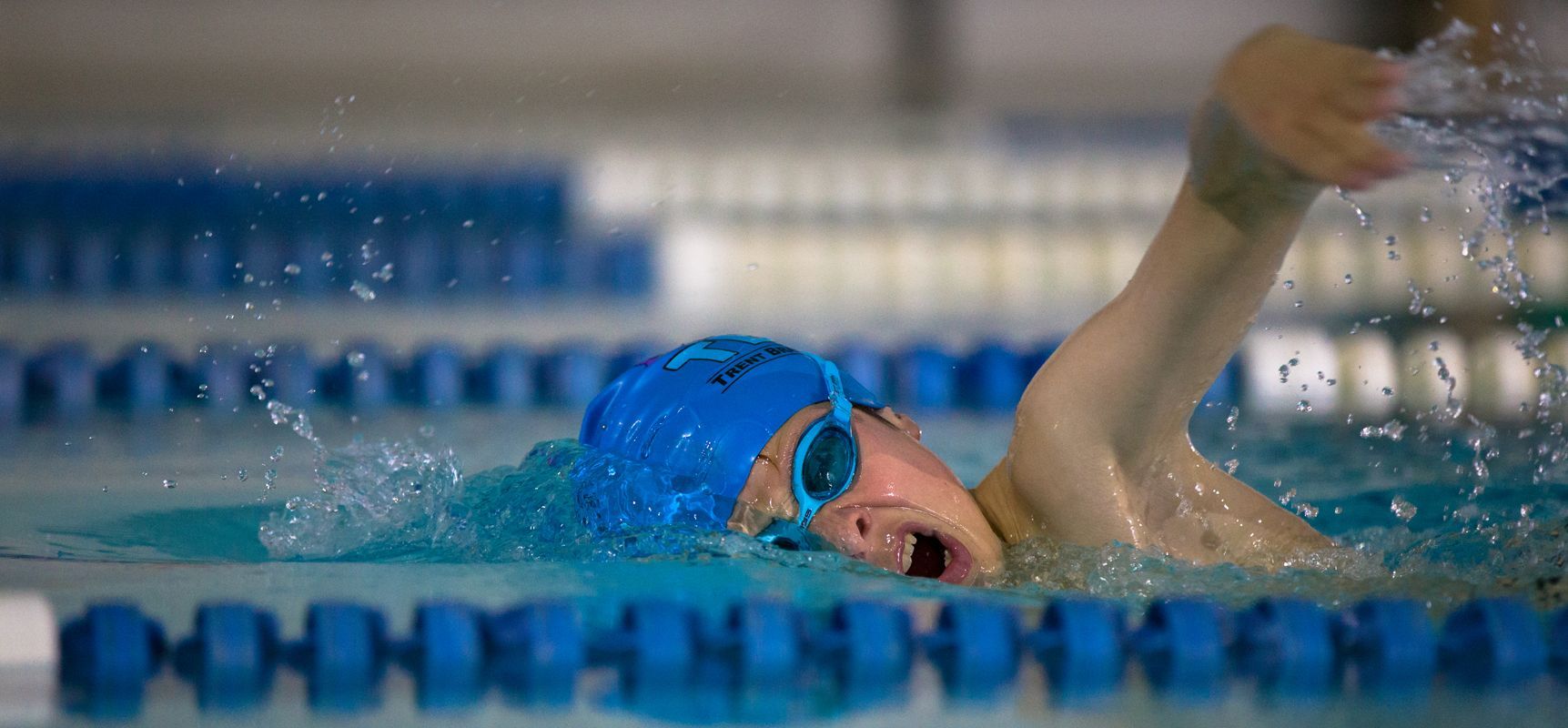 A young boy is swimming in a swimming pool wearing a blue cap and goggles.