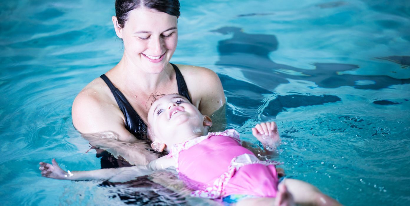 A woman is teaching a baby how to swim in a swimming pool.