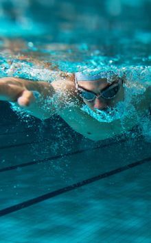 A man is swimming in a swimming pool wearing goggles.