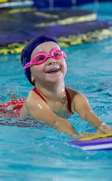 A little girl is swimming in a pool wearing goggles and a hat.