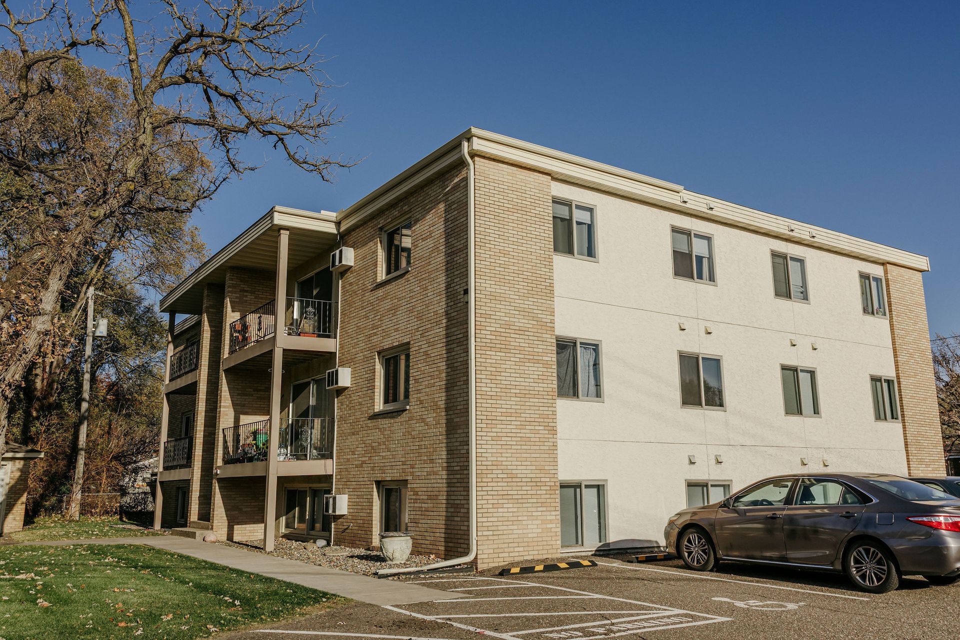 Three-story apartment building with parked cars and trees on a sunny day