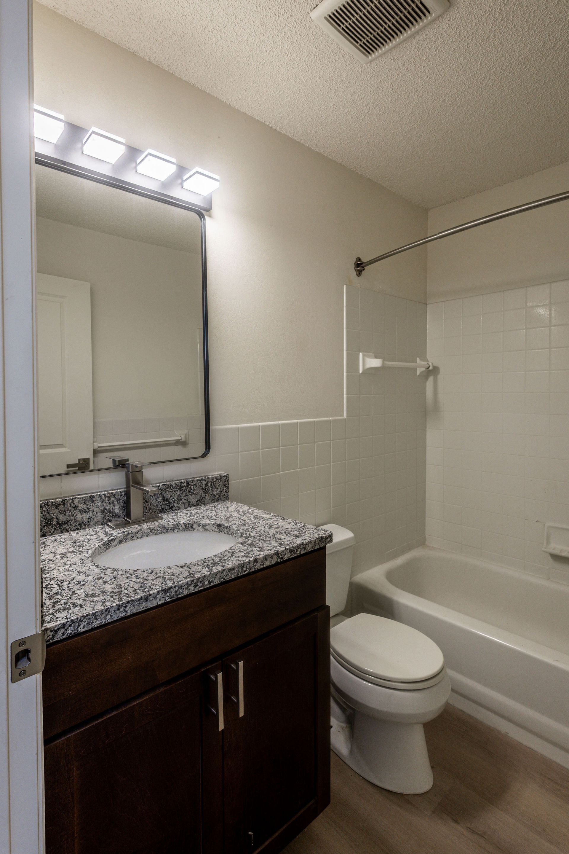 Small bathroom with dark wood vanity, granite countertop, mirror, toilet, and bathtub/shower.