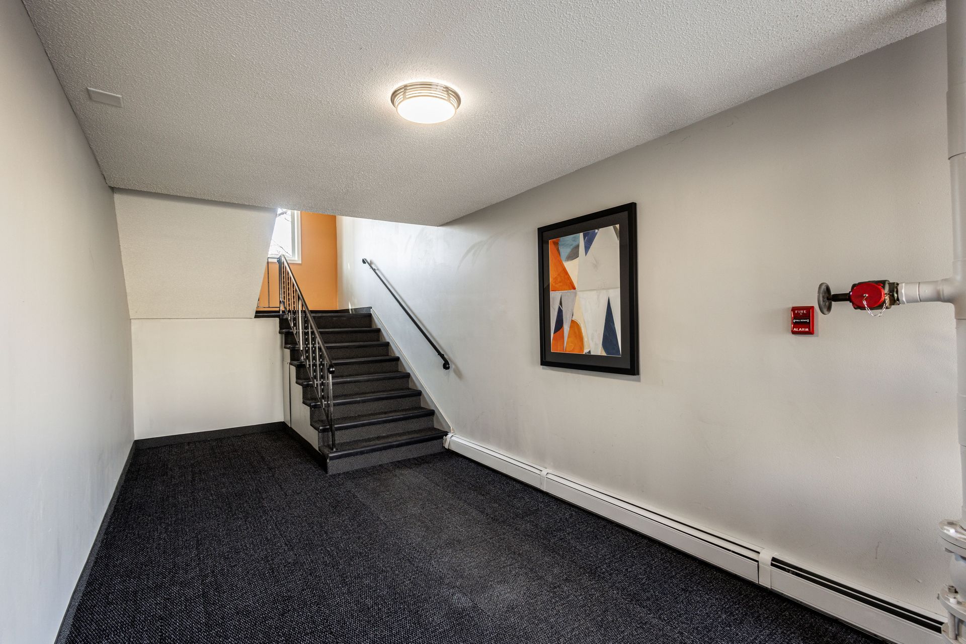 Empty hallway with staircase, white walls, dark carpet, and framed wall art
