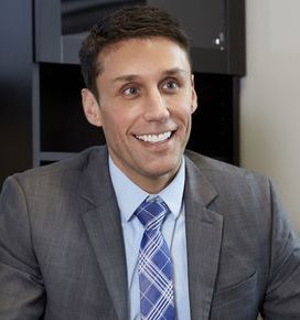 A man in a suit and tie is smiling while sitting at a desk.