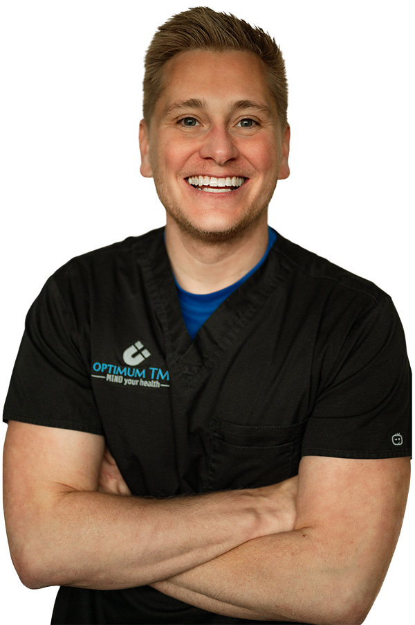 A man in a black scrub top is smiling with his arms crossed.