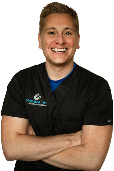 A man in a black scrub top is smiling with his arms crossed.