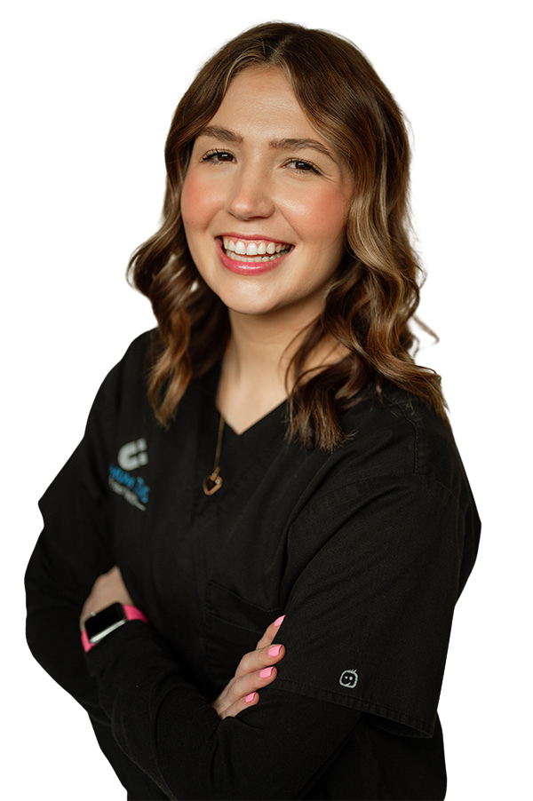 A woman in a black scrub top is smiling with her arms crossed.