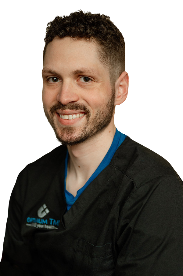 A man with a beard is wearing a black scrub top and smiling.