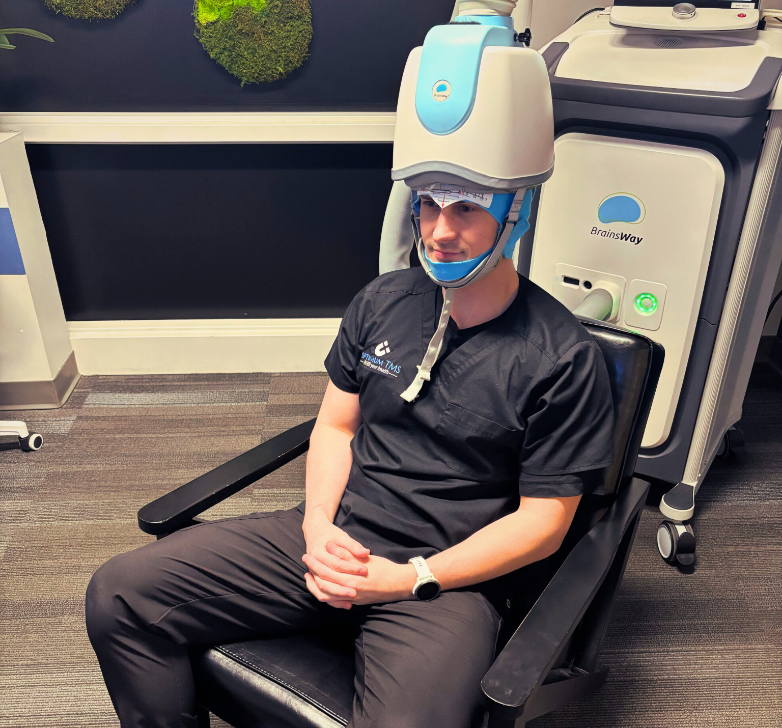 Person seated in a clinic chair wearing a blue and clear head-mounted device with a chin strap