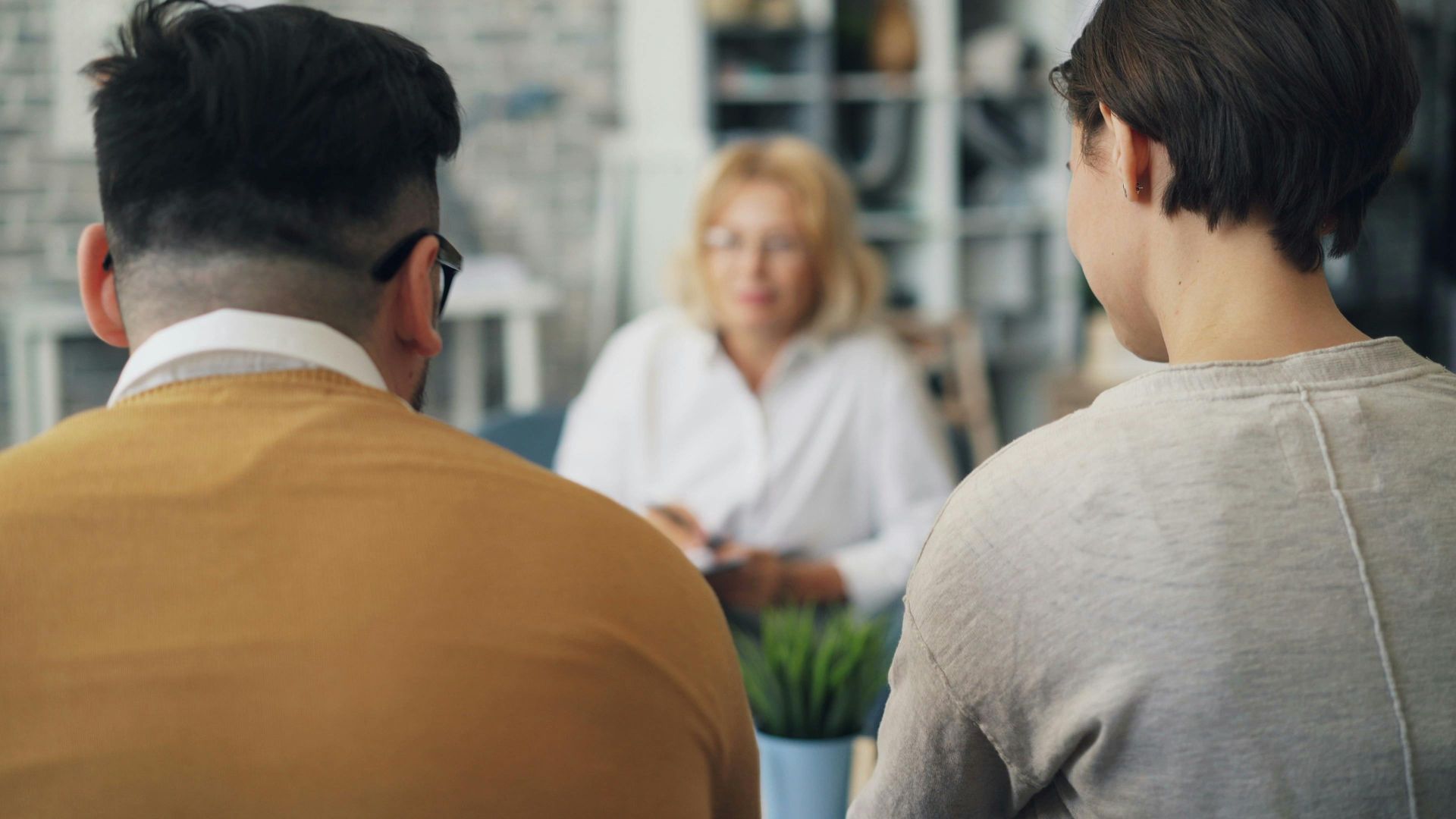 Two people seen from behind talking with a woman seated across the table in a bright office meeting room