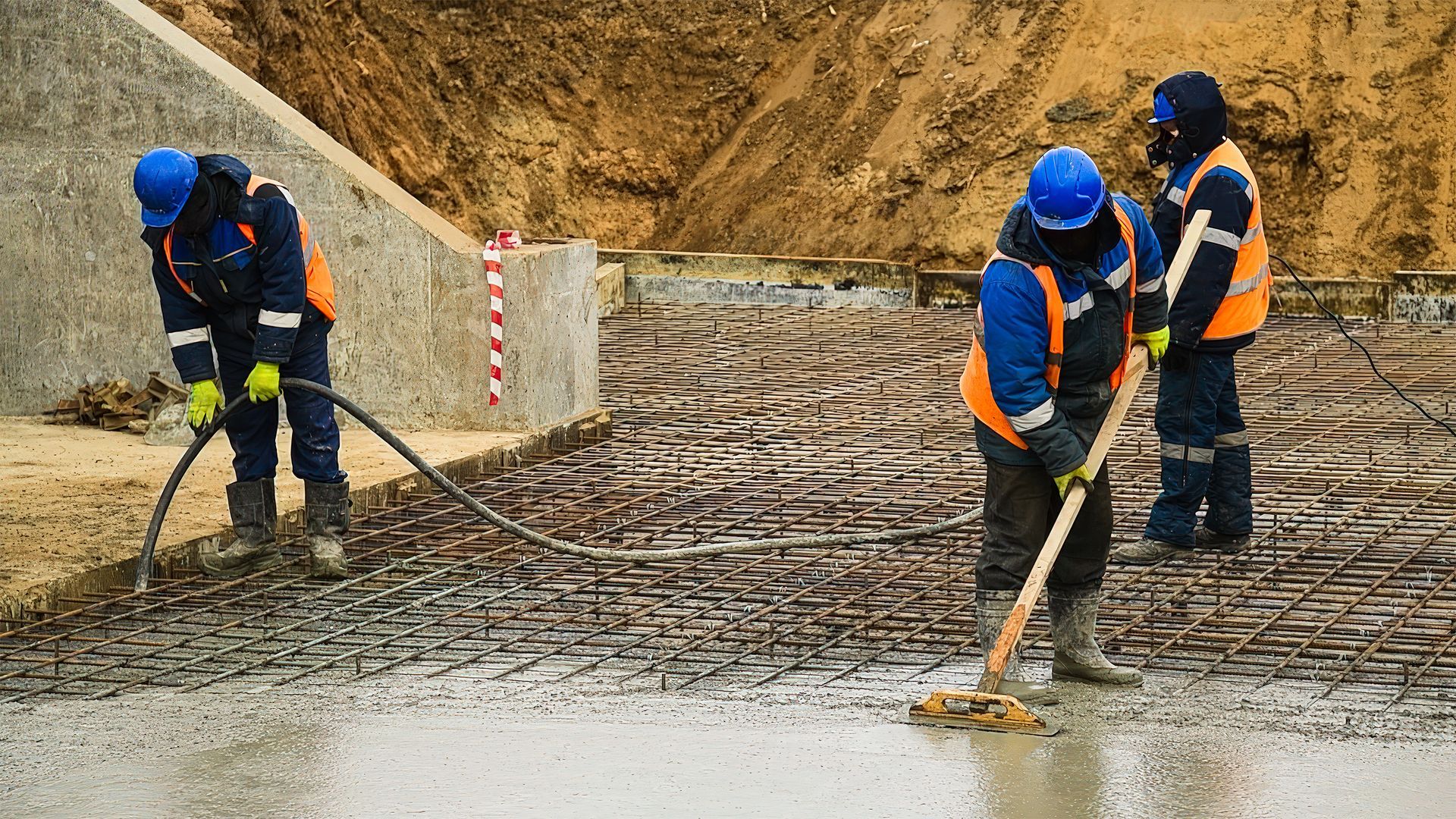 Construction workers pouring and leveling wet concrete on a rebar-covered surface; outdoor setting.