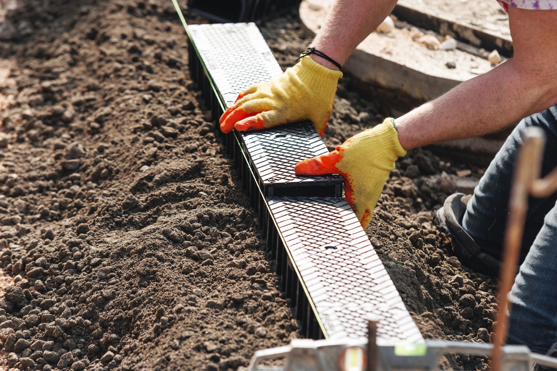 Person in yellow gloves installing a black plastic landscape edging in soil.