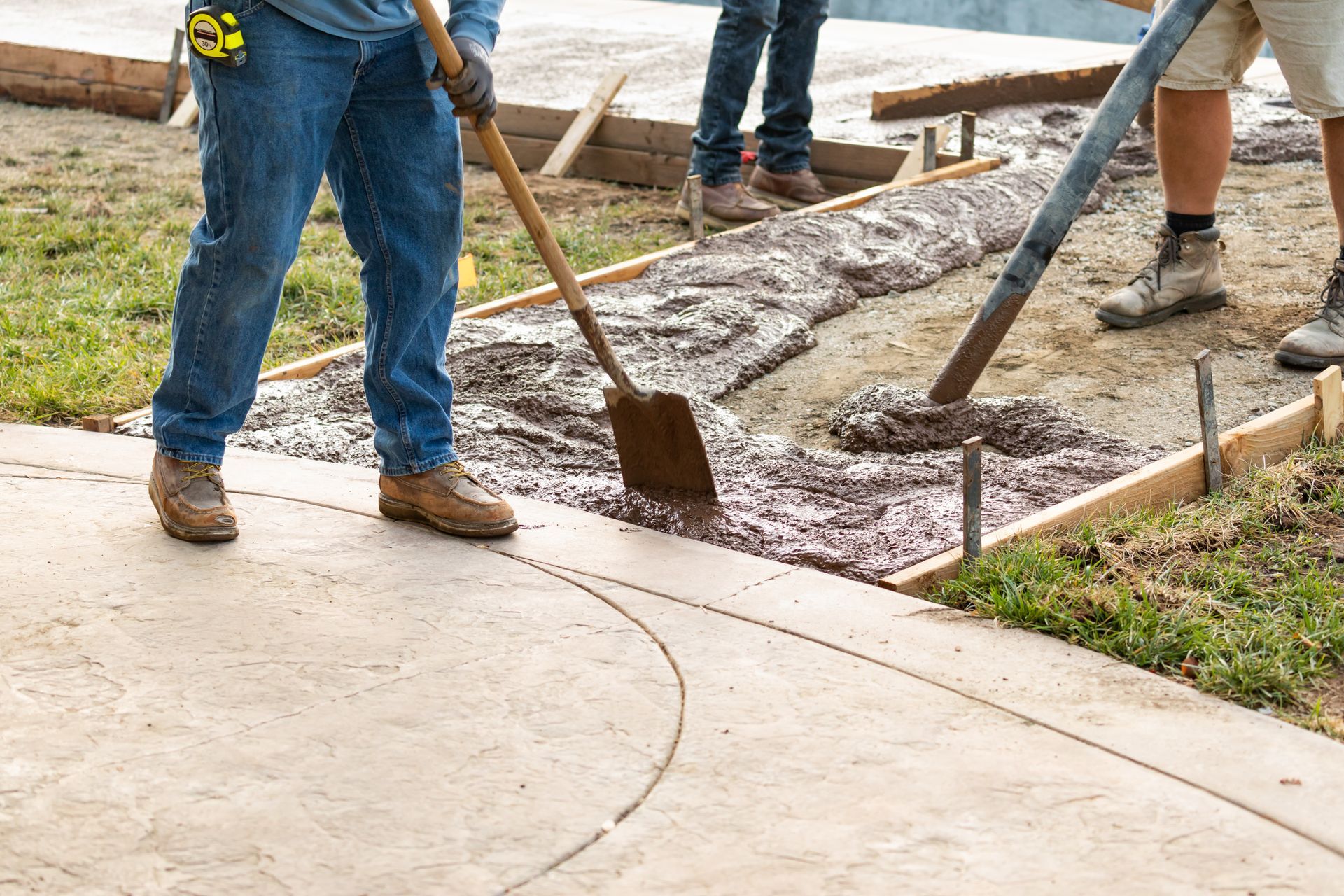Workers spreading concrete with shovels and a hose in an outdoor construction area.