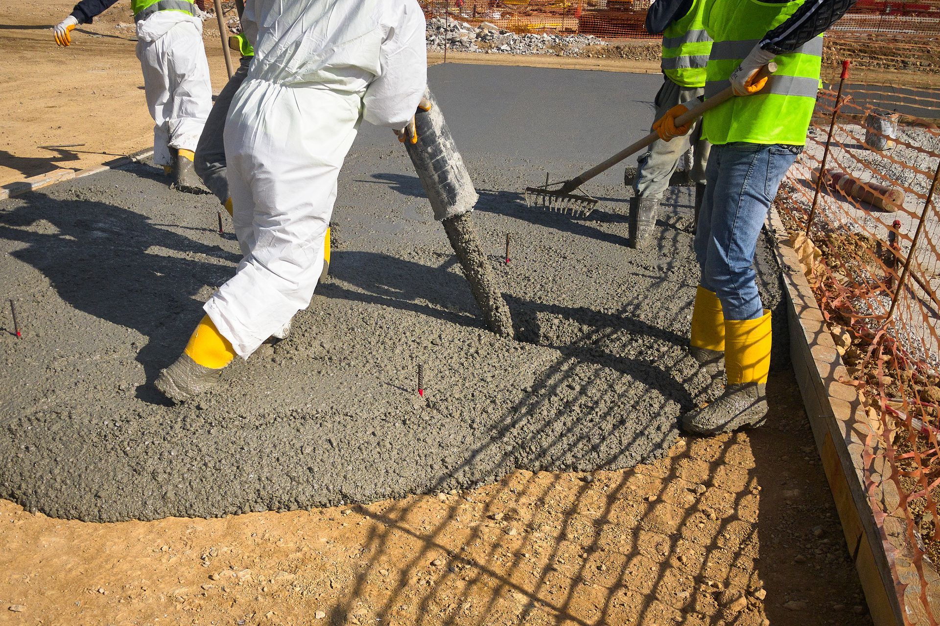 Construction workers pouring and leveling wet concrete on a road surface.
