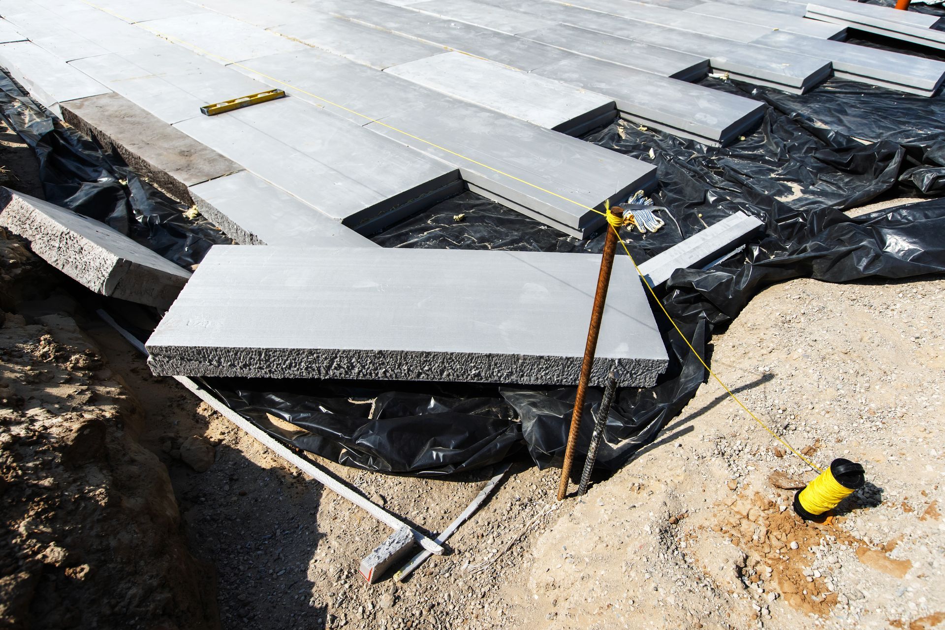 Construction site with rectangular gray concrete pavers being installed.