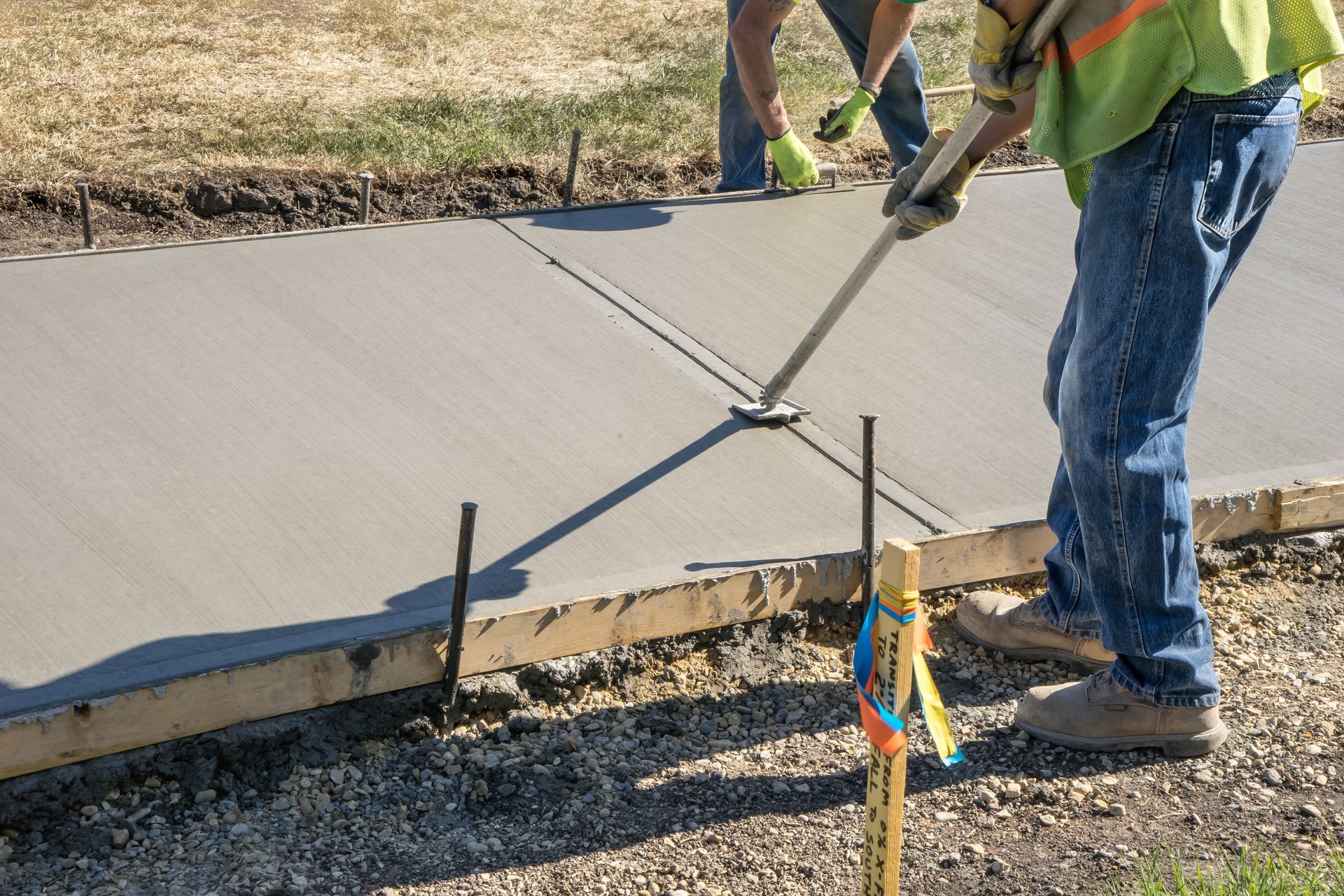 Construction workers smoothing wet concrete sidewalk with hand tools.