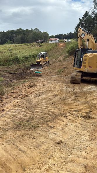 Yellow heavy construction machinery working on an unpaved, hilly dirt terrain under a cloudy sky.