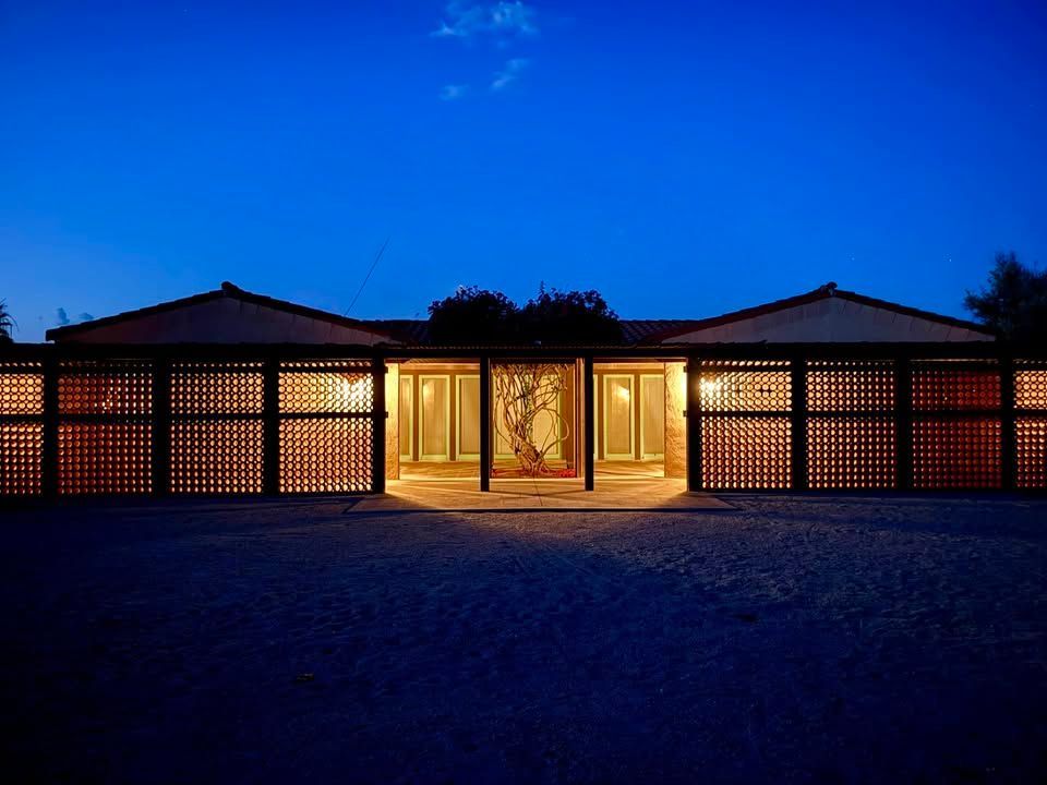 A one-story home with a lattice exterior facade and warm interior lighting under a deep blue twilight sky.