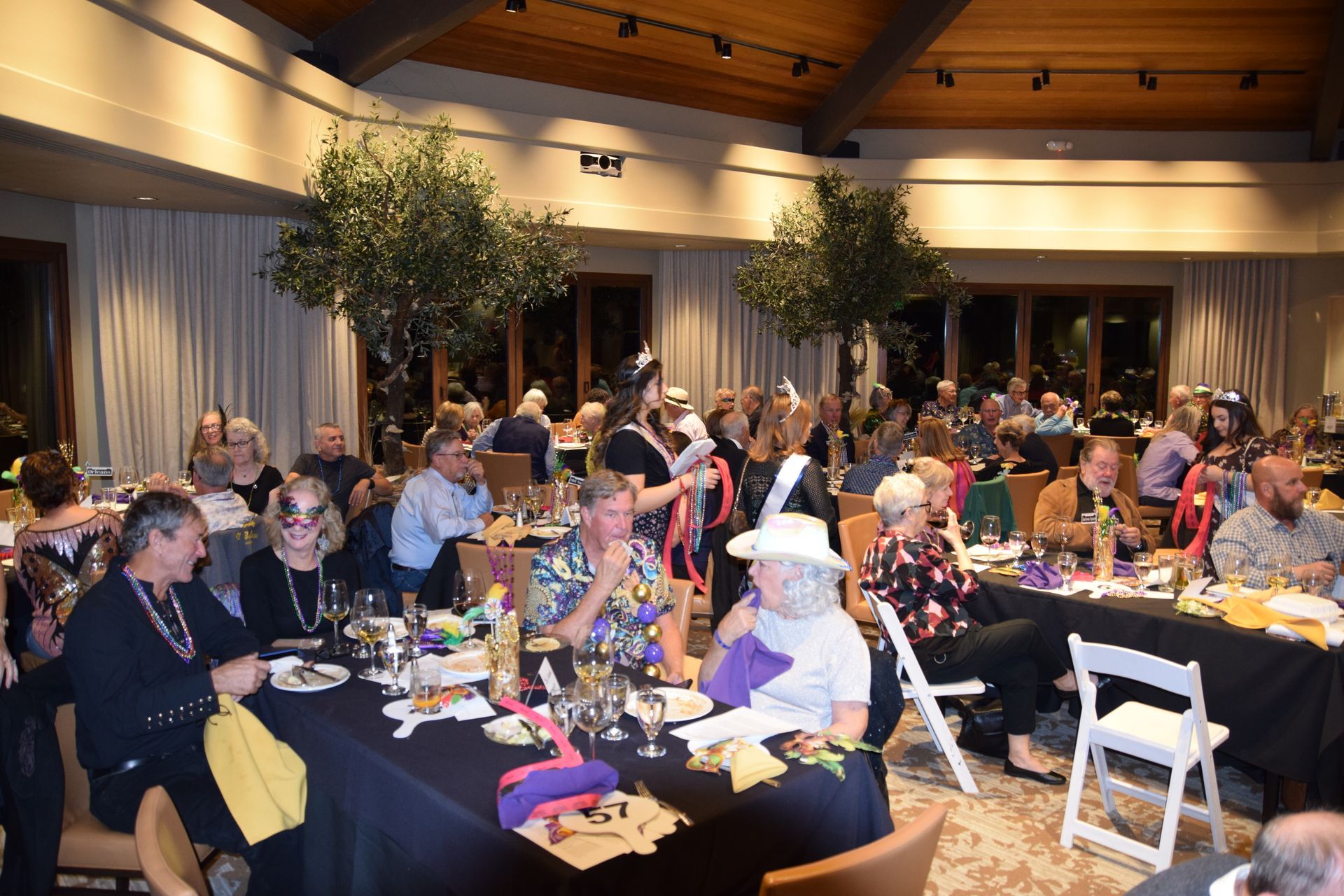 A banquet hall with guests seated at tables covered in black tablecloths during a social evening event.