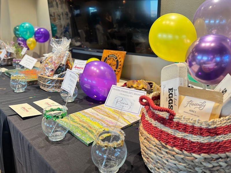 A raffle or auction table with gift baskets, small bowls, cards, and colorful balloons.