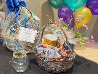 Two gift baskets with wrapped items and a small decorative glass bowl sit on a dark surface near colorful balloons.
