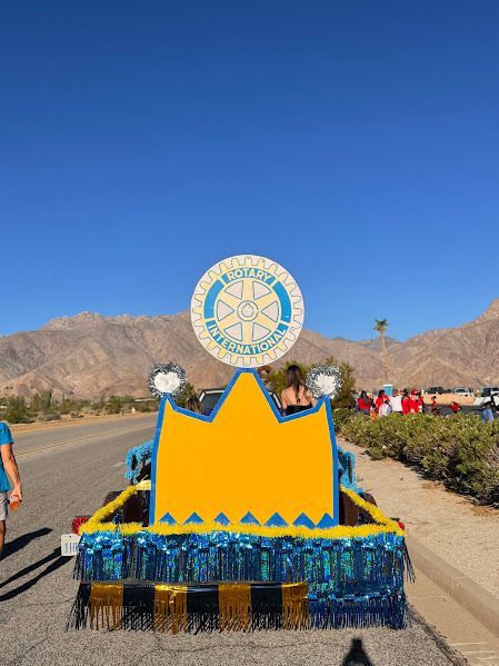 A parade float featuring a large, yellow crown cutout topped with a circular Lions Club International sign against a desert.
