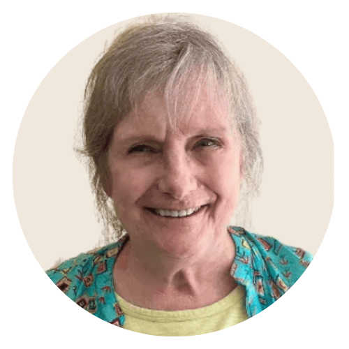 A smiling person with shoulder-length hair wearing a yellow shirt under an unbuttoned turquoise patterned vest.