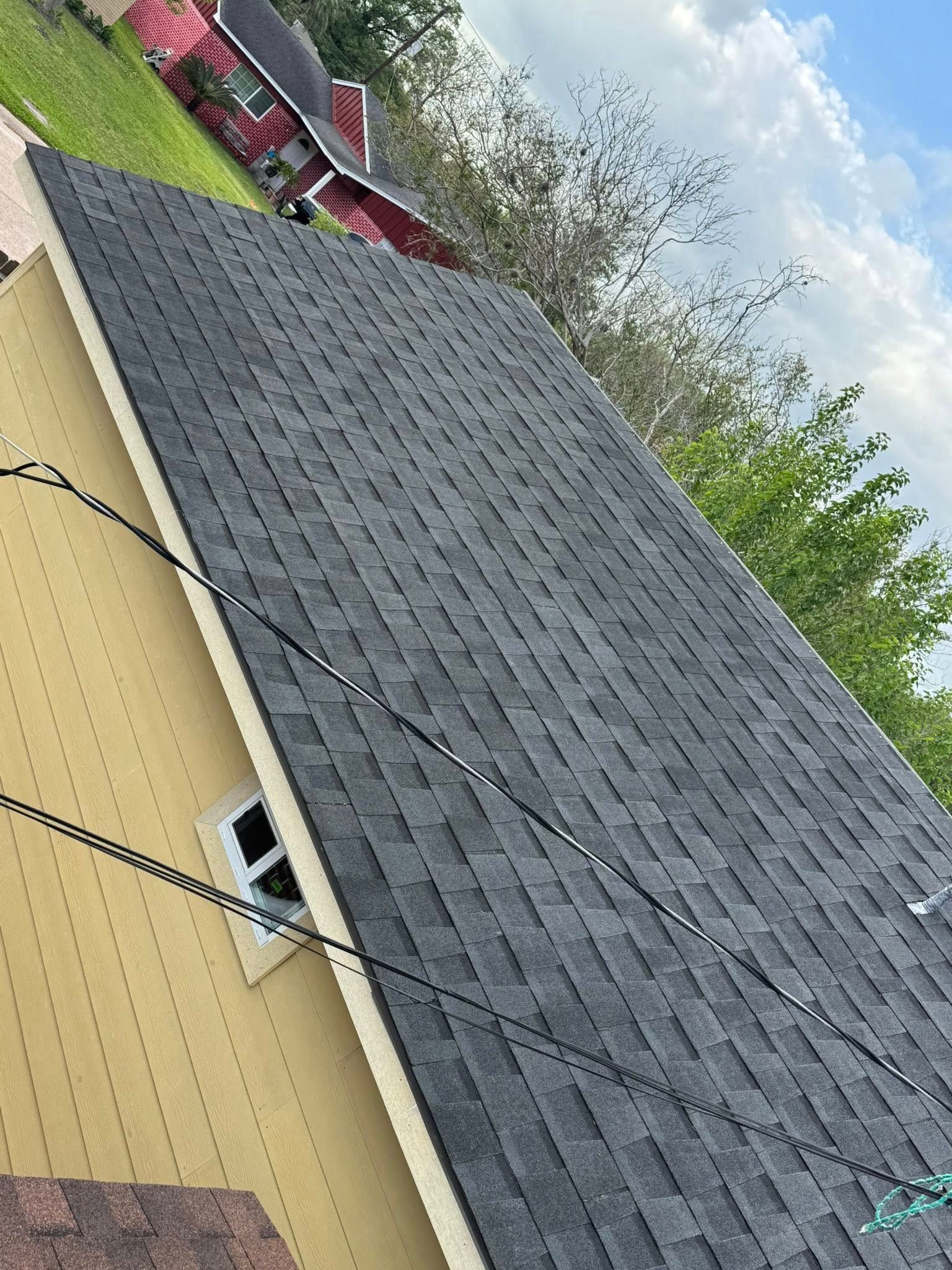 Dark shingled roof on a yellow house, viewed at an angle with trees and a red truck in the background
