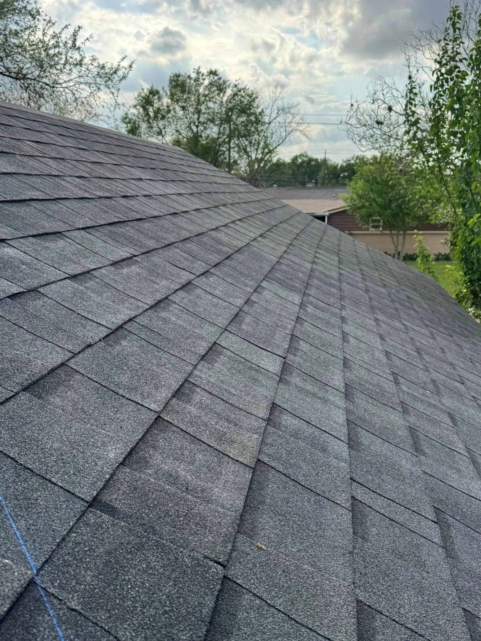 Gray shingled roof slopes down under a cloudy sky with trees in the background