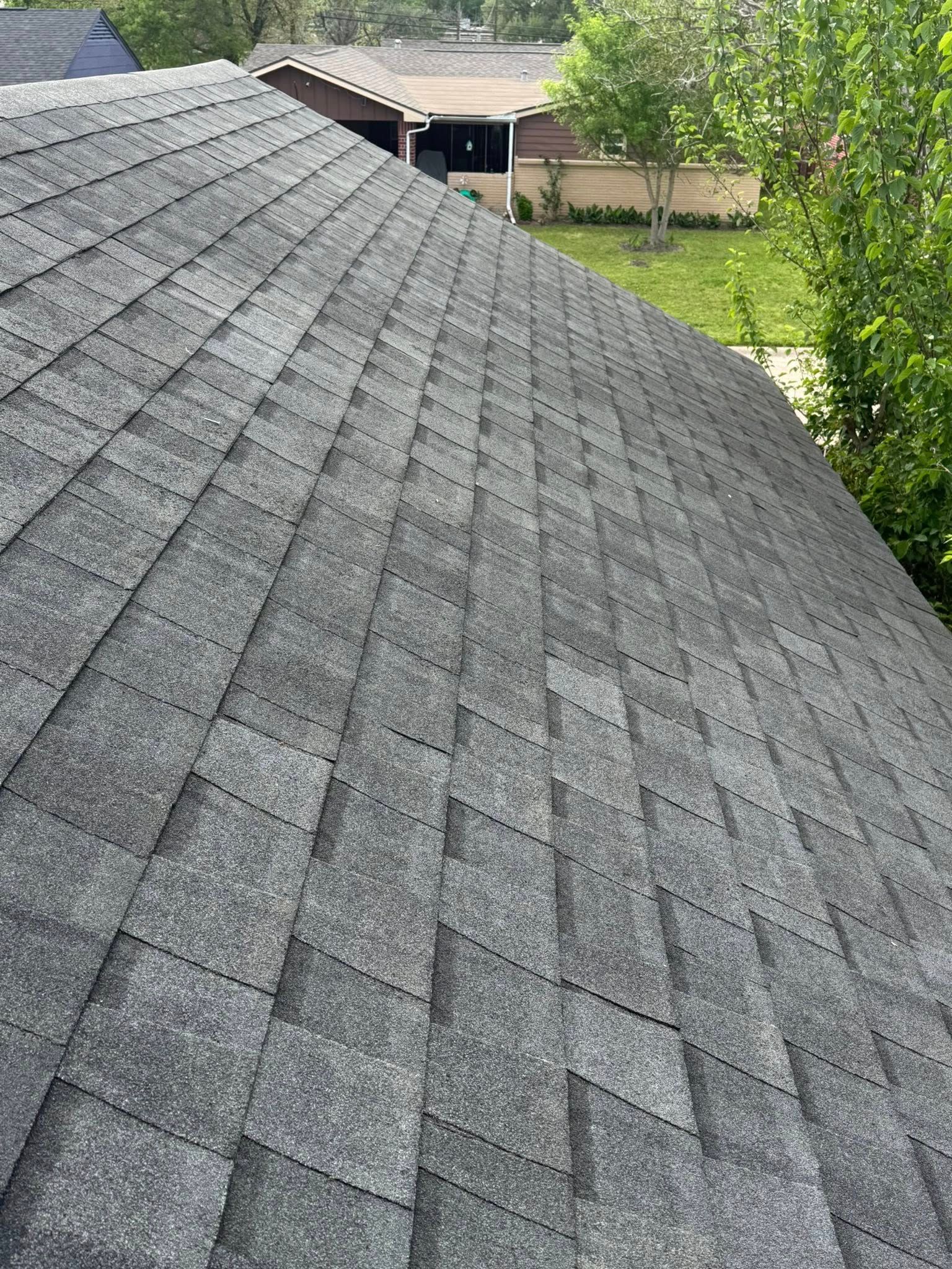 Gray shingled roof with trees and a backyard visible beyond the ridge