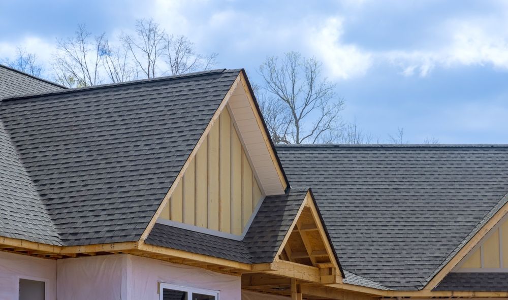 Close-up of residential roof gables with gray shingles and beige siding under a partly cloudy sky
