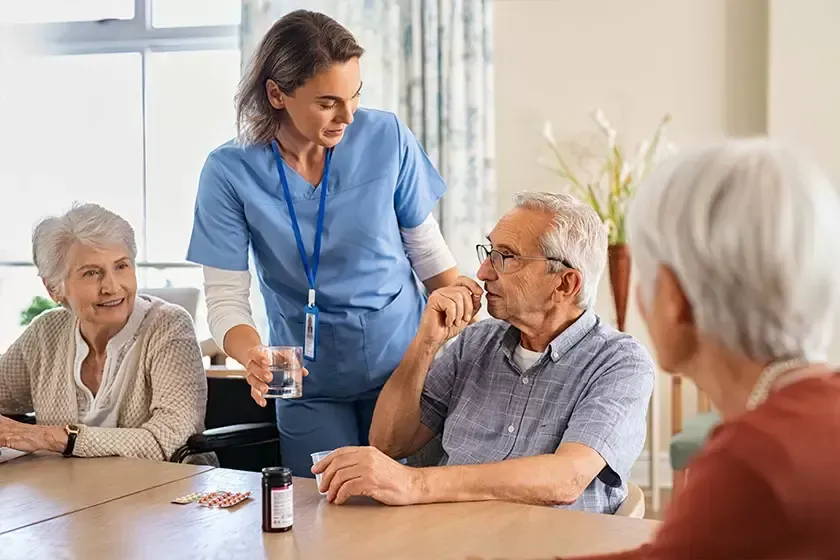 A nurse is giving an elderly man a glass of water.