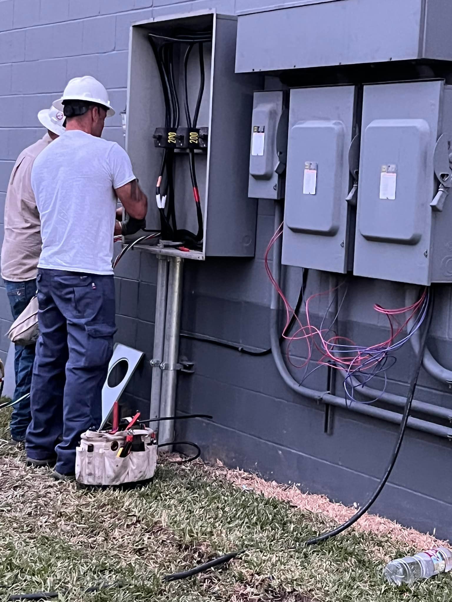 Two electricians working on electrical boxes outdoors.