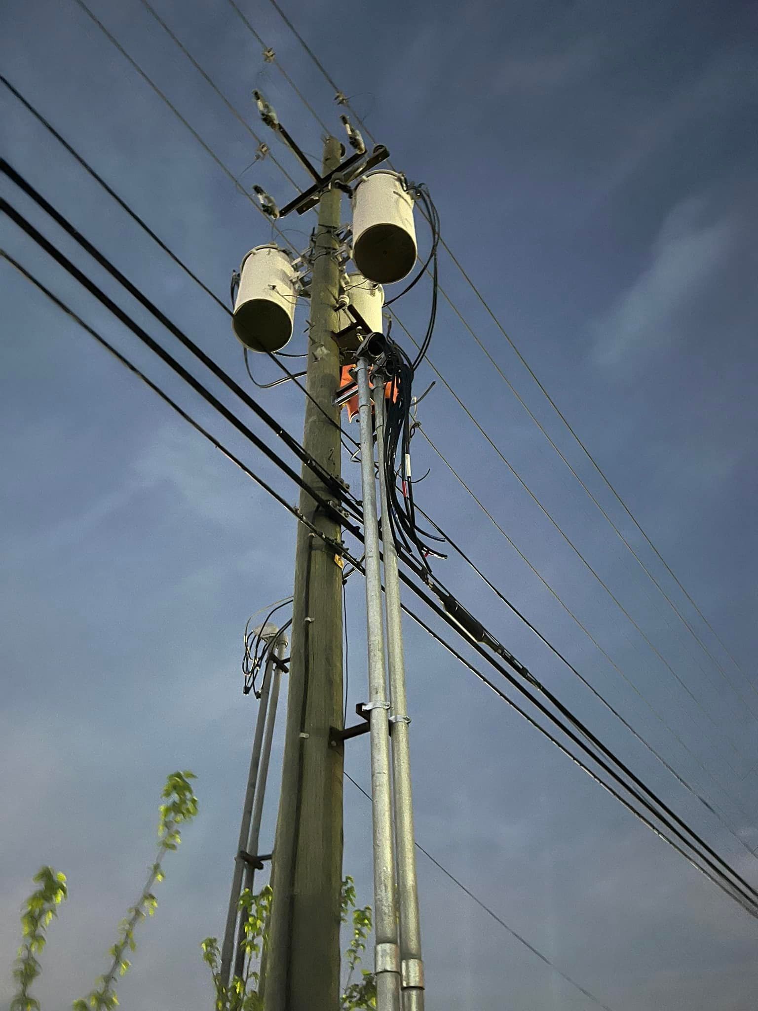 Lineman on a utility pole with transformers and wires against a cloudy sky.