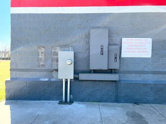 Electrical boxes on a gray brick wall with a red and white stripe above. A sign is to the right.
