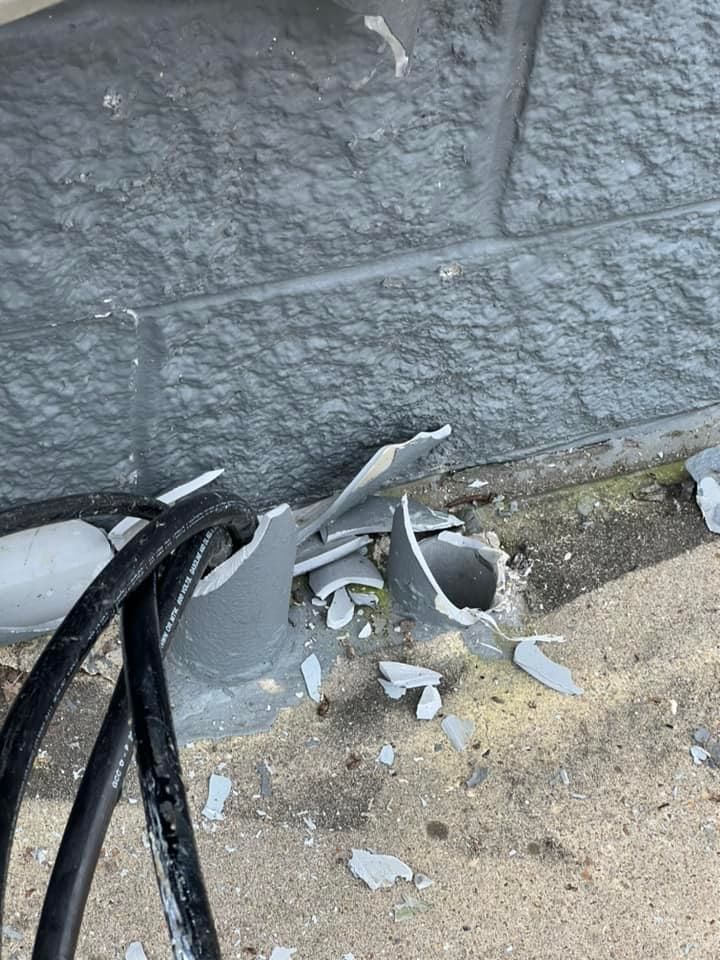 Broken gray conduit with black cables against a gray textured wall. Debris is scattered on the ground.