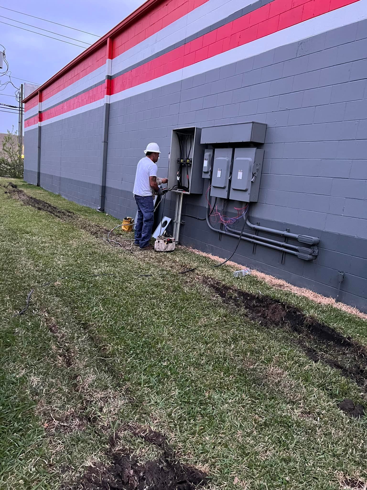 Man in hard hat working on electrical box on the side of a building.