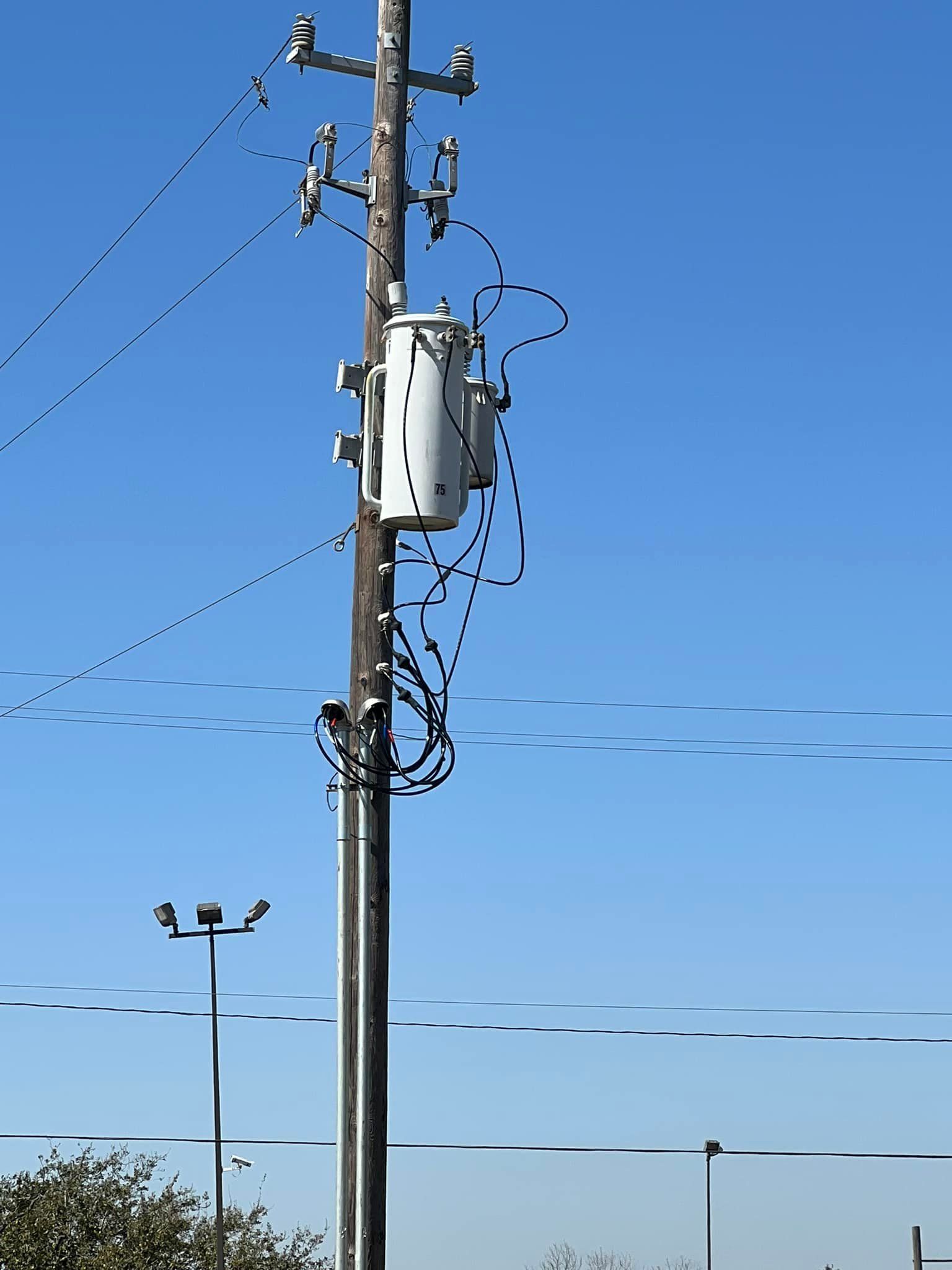 Power pole with transformer, wires against a blue sky.