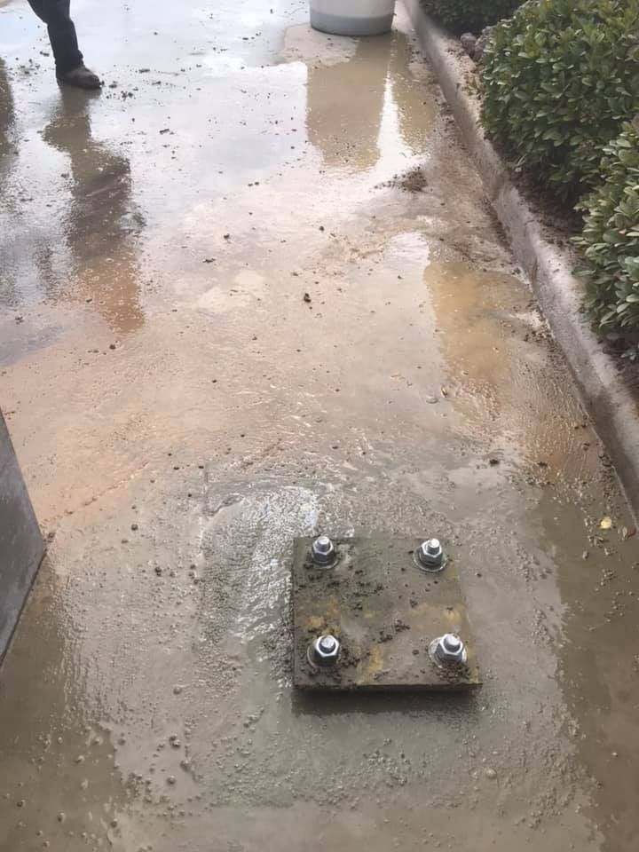 Wet concrete sidewalk with a metal plate bolted to the ground; a person's legs are visible.