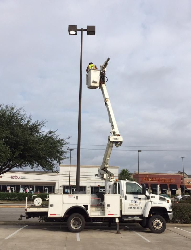 A worker in a bucket truck repairs a street light in a parking lot on a cloudy day.